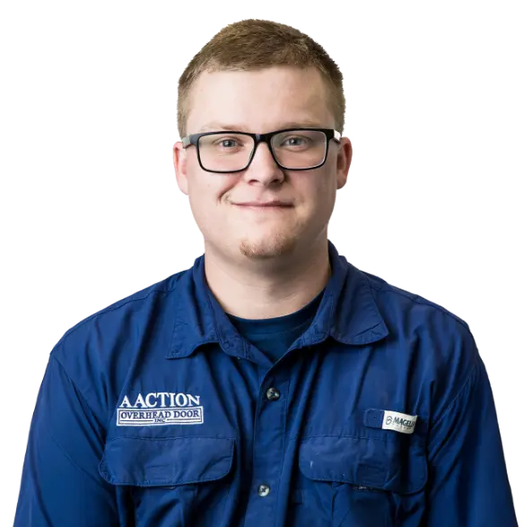 A young man with short light brown hair, wearing black glasses and a blue work shirt with A Action Overhead Door and Magnum logos, smiles at the camera against a white background.