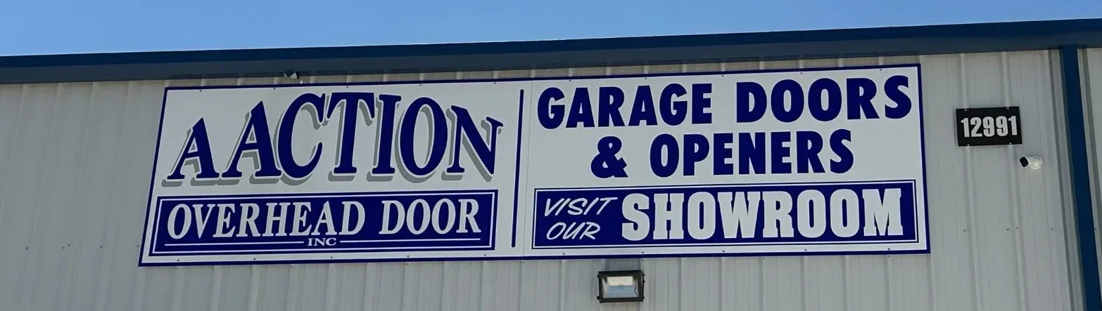 A large sign on a building reads: A Action Overhead Door Inc. Garage Doors & Openers. Visit Our Showroom. The address number 12901 is posted on the wall.