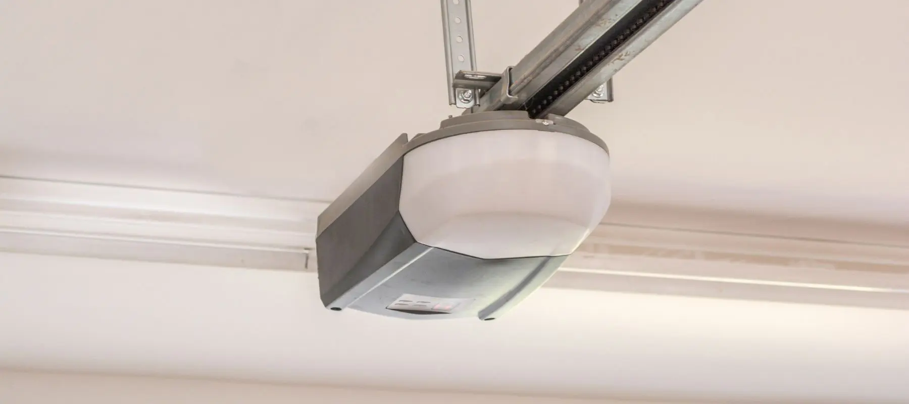 Close-up view of an automatic garage door opener mounted on the ceiling, with a metal rail extending from the device.