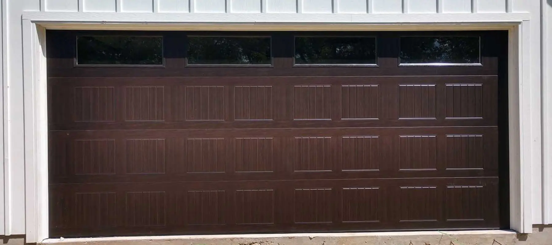 A closed brown garage door with four rectangular windows at the top, set in a white exterior wall.